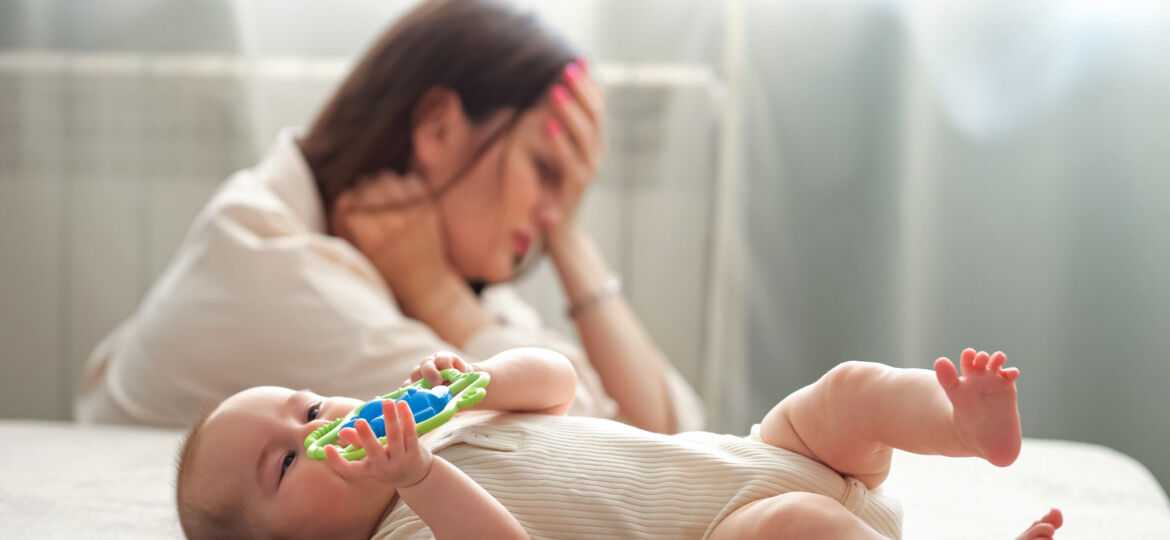 Delighted baby girl plays with toys against tired mother